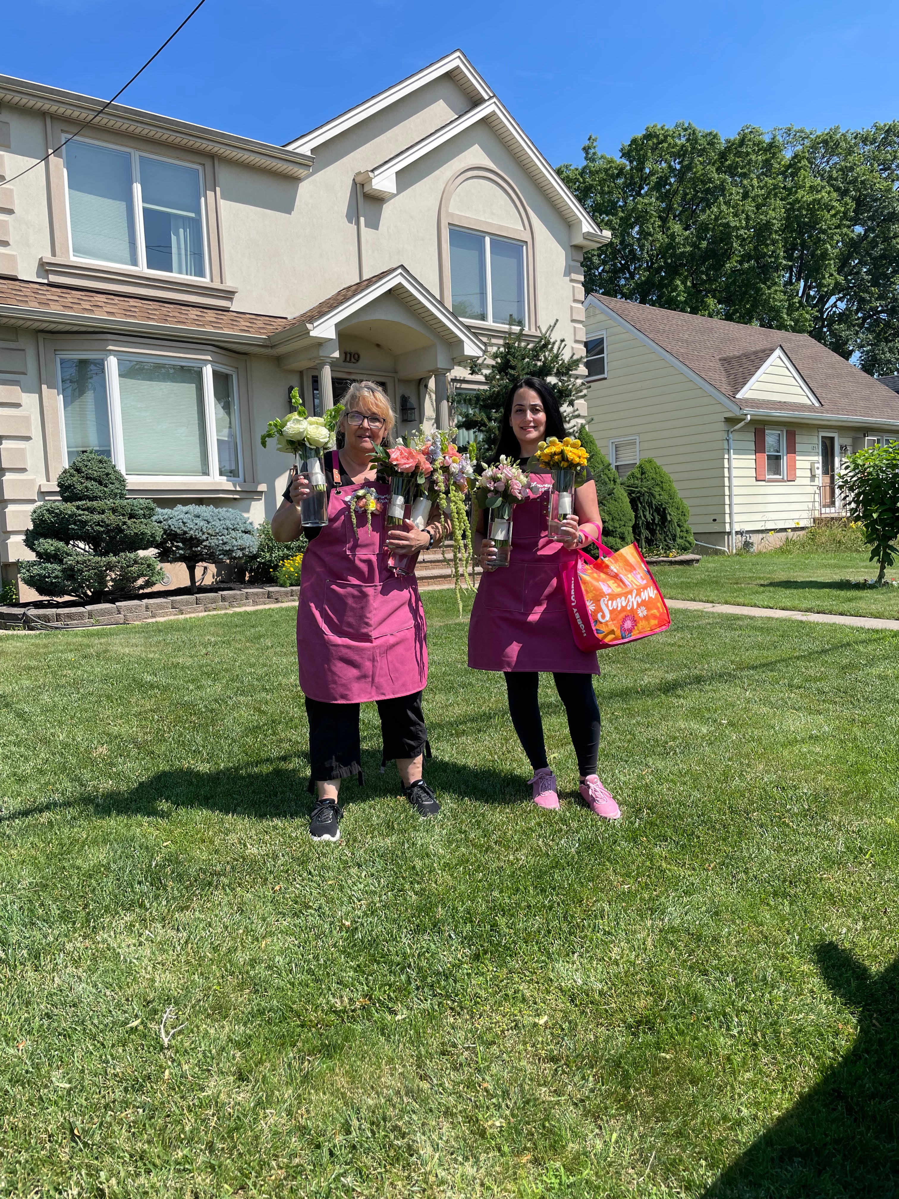 Two women in pink aprons standing in a grassy area with houses in the background